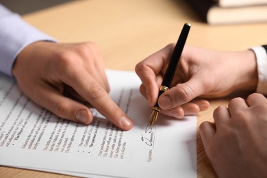 Photo of Man pointing at document and woman putting signature at table, closeup