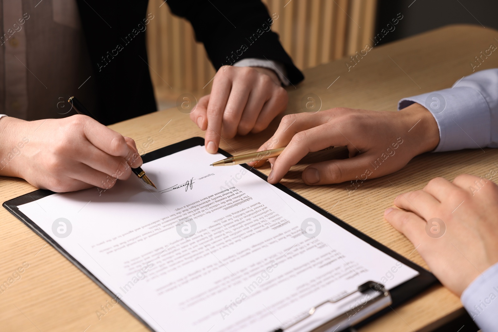 Photo of Man pointing at document and woman putting signature at wooden table, closeup