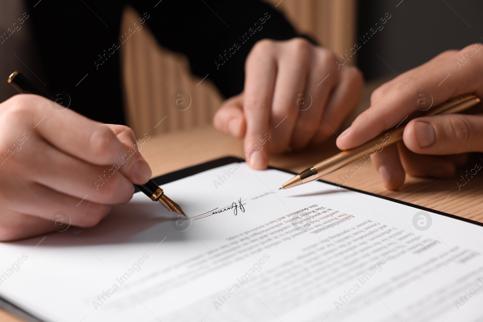 Photo of Man pointing at document and woman putting signature at table, closeup