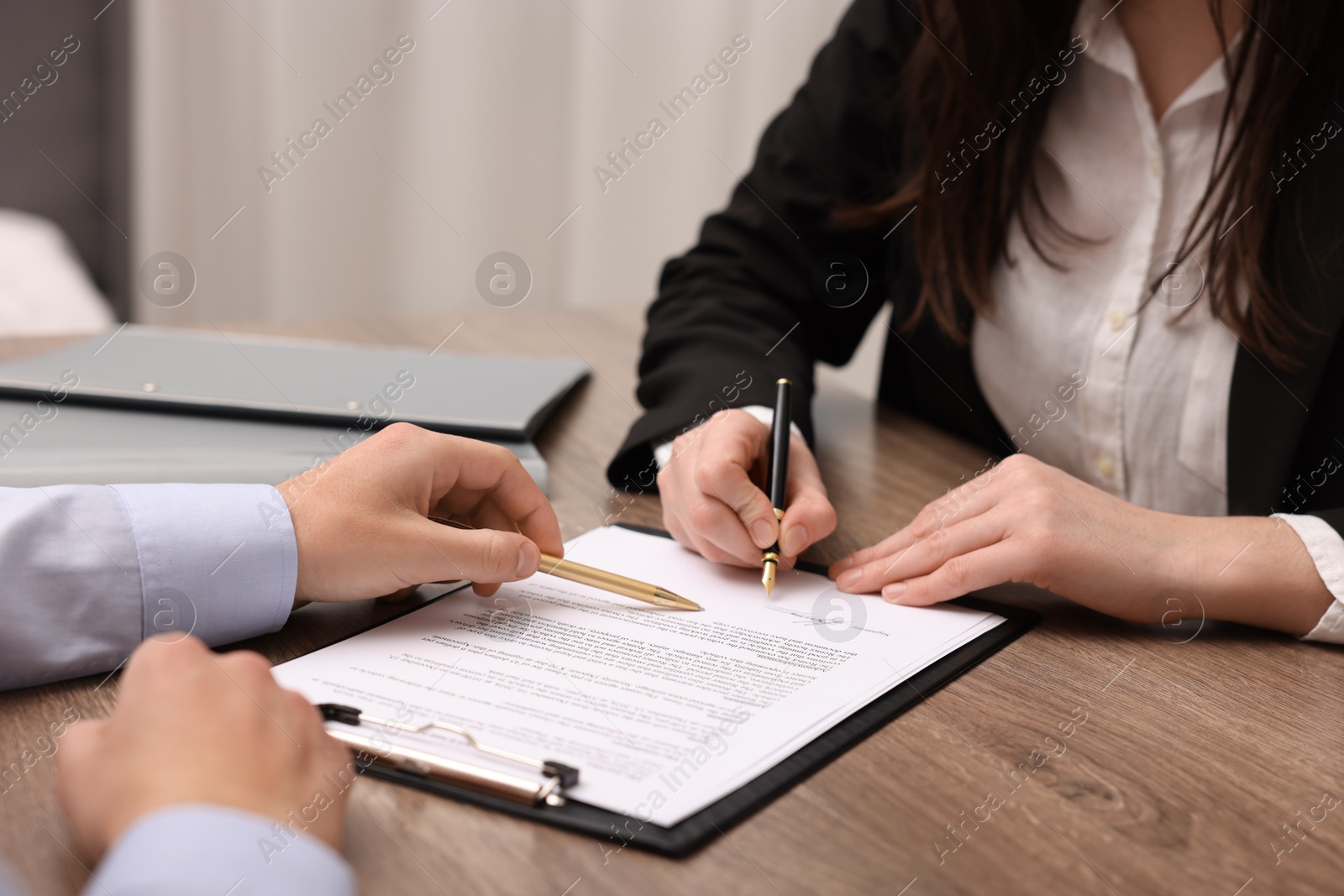 Photo of Man pointing at document and woman putting signature at wooden table, closeup