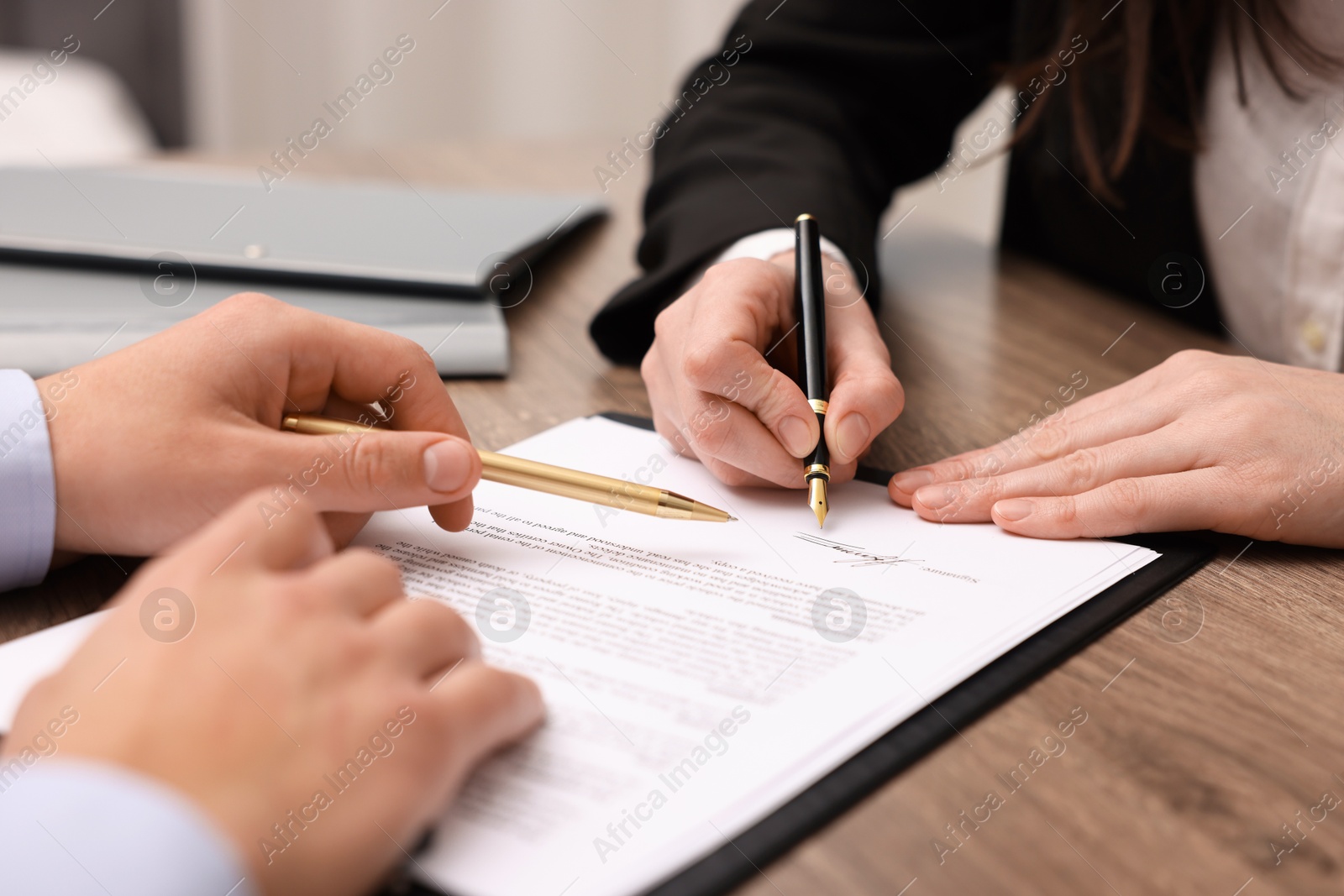 Photo of Man pointing at document and woman putting signature at wooden table, closeup