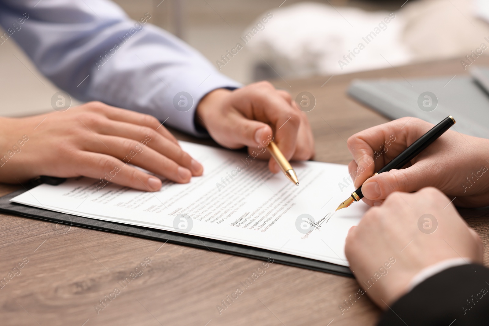 Photo of Man pointing at document and woman putting signature at wooden table, closeup