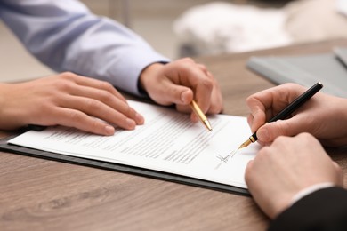 Photo of Man pointing at document and woman putting signature at wooden table, closeup