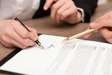 Photo of Man pointing at document and woman putting signature at table, closeup