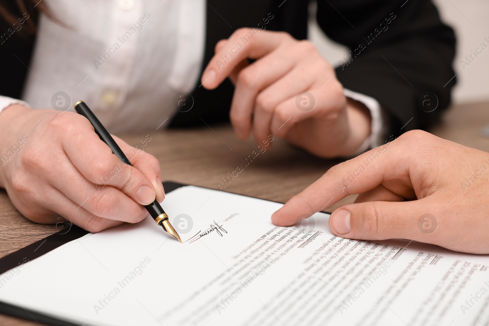 Photo of Man pointing at document and woman putting signature at table, closeup