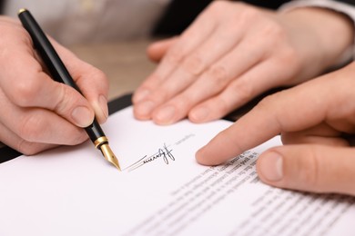 Photo of Man pointing at document and woman putting signature at table, closeup