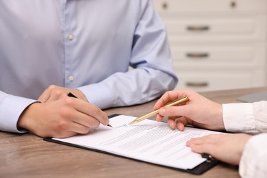 Photo of Woman pointing at document and man putting signature at wooden table, closeup