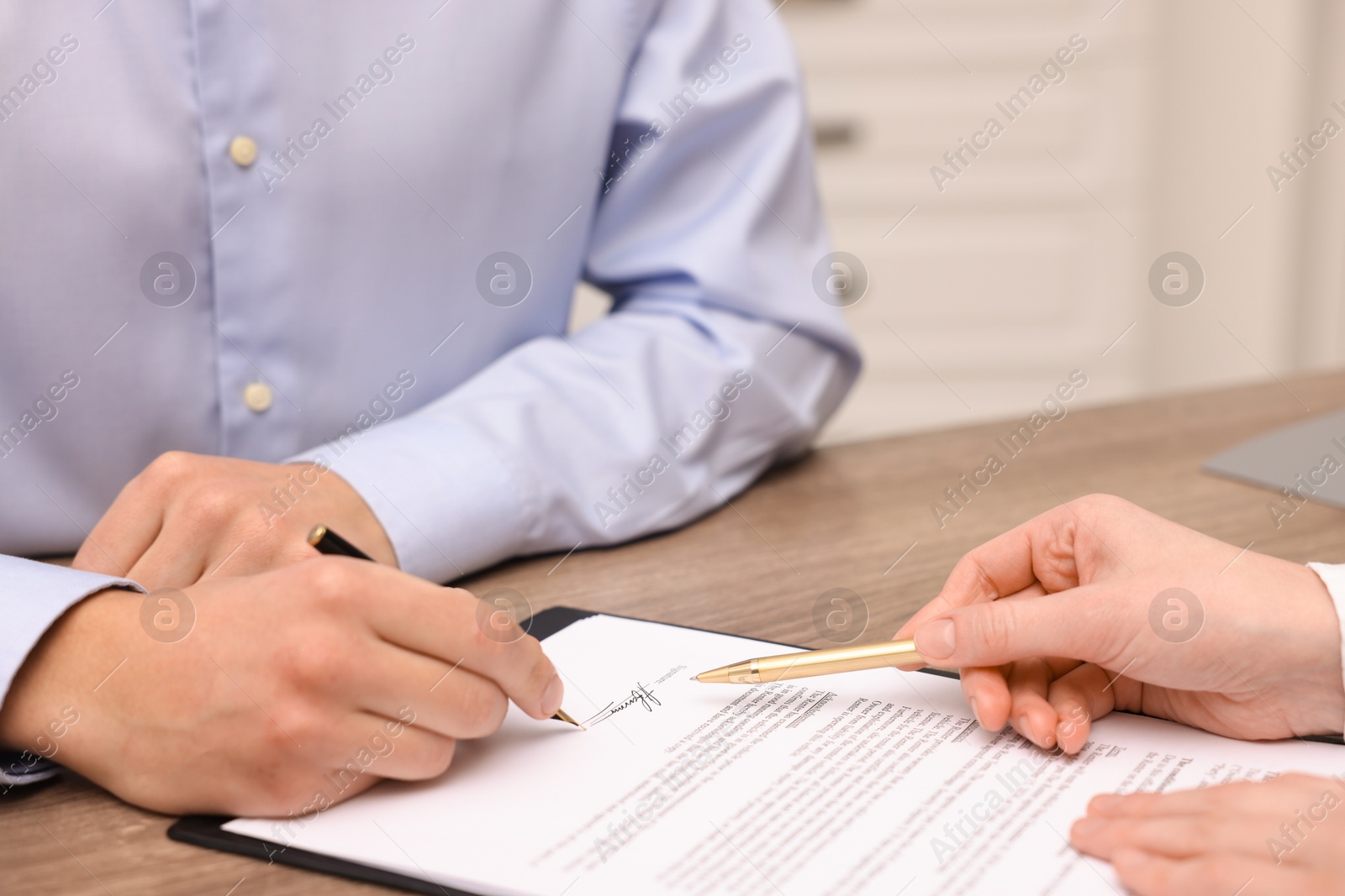 Photo of Woman pointing at document and man putting signature at table, closeup