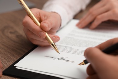 Photo of Woman pointing at document and man putting signature at wooden table, closeup