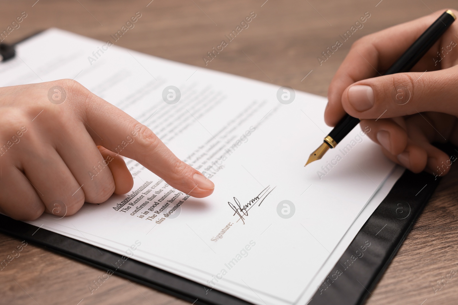 Photo of Woman pointing at document and man putting signature at wooden table, closeup