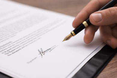 Photo of Man putting signature on document at table, closeup