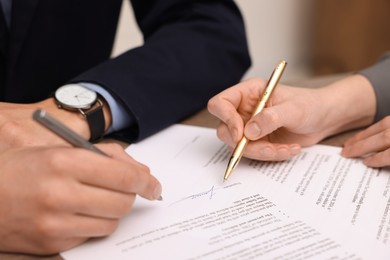 Photo of Woman pointing at document and man putting signature at table, closeup