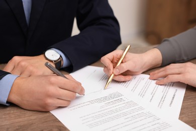 Photo of Woman pointing at document and man putting signature at wooden table, closeup