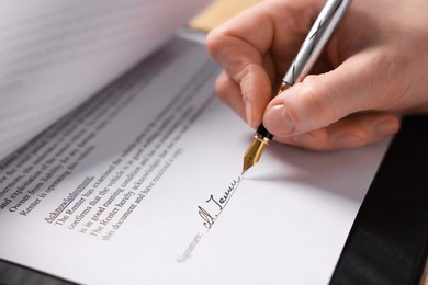 Photo of Woman putting signature on document at table, closeup