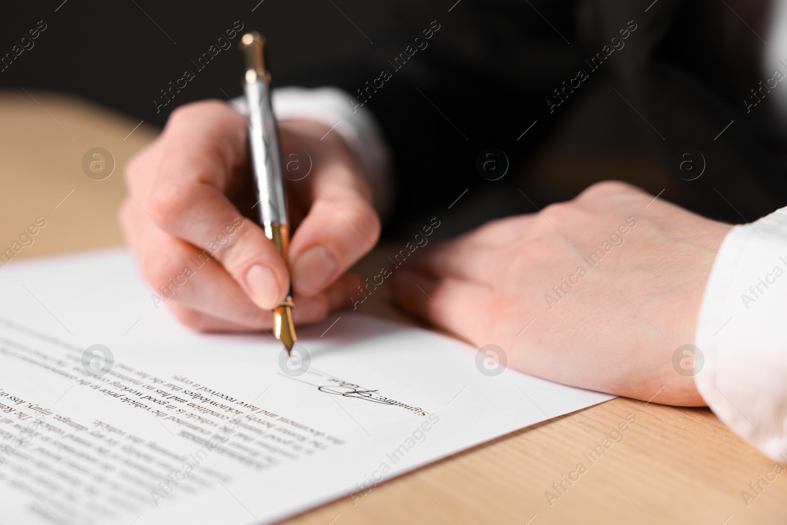 Photo of Woman putting signature on document at wooden table, closeup