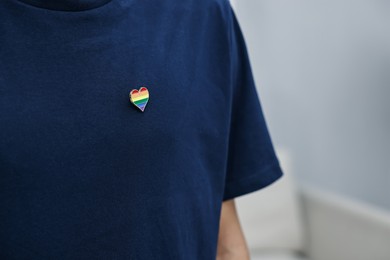 Photo of Man with heart shaped pin in colors of LGBT flag indoors, closeup