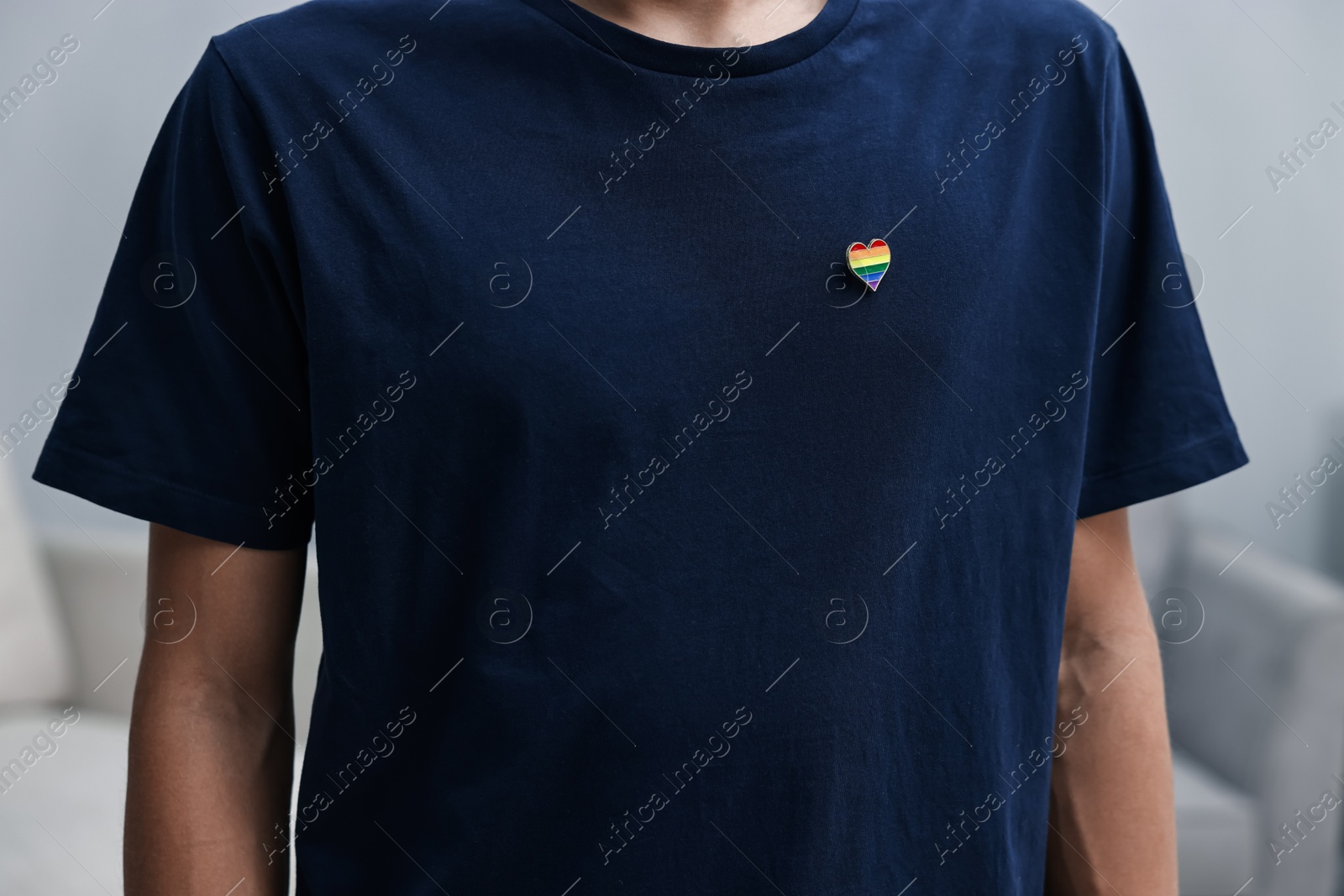 Photo of Man with heart shaped pin in colors of LGBT flag indoors, closeup