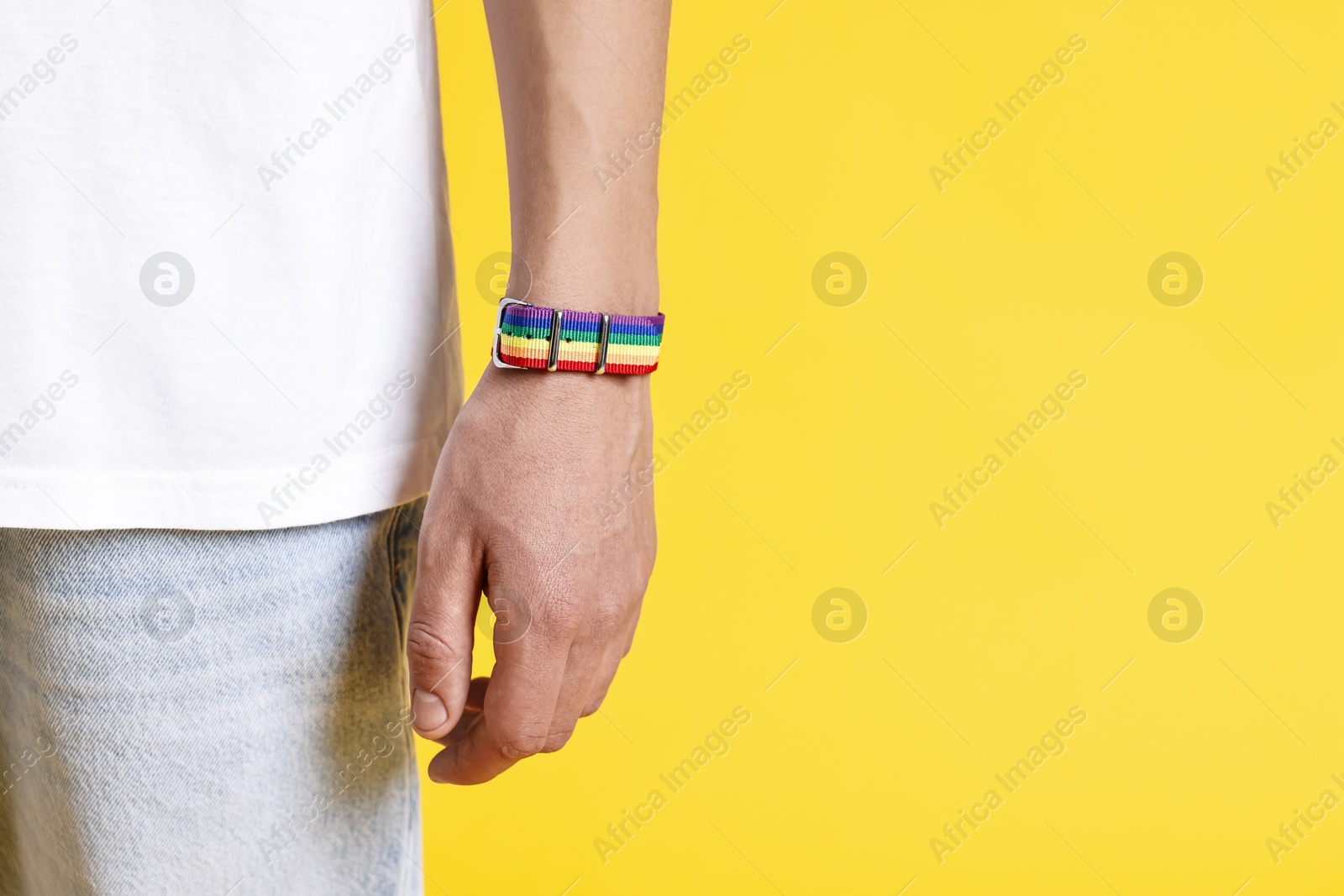 Photo of Man with bracelet in colors of LGBT flag on yellow background, closeup. Space for text