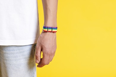 Photo of Man with bracelet in colors of LGBT flag on yellow background, closeup. Space for text