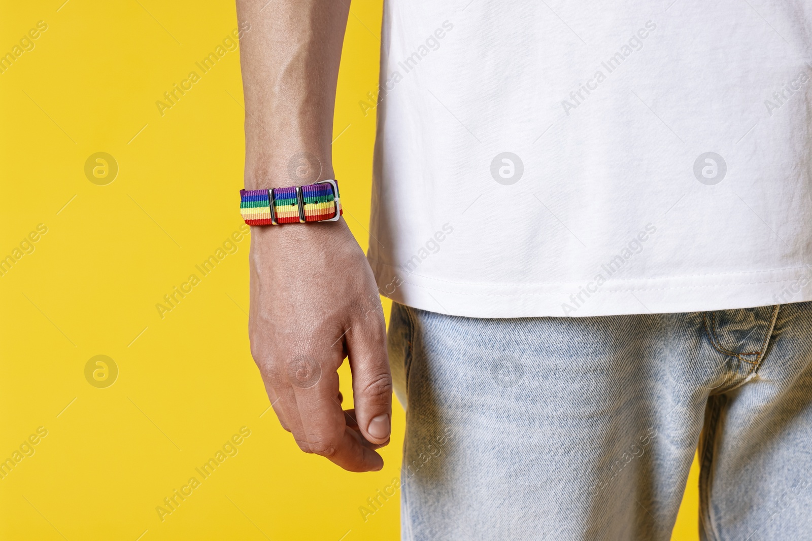 Photo of Man with bracelet in colors of LGBT flag on yellow background, closeup