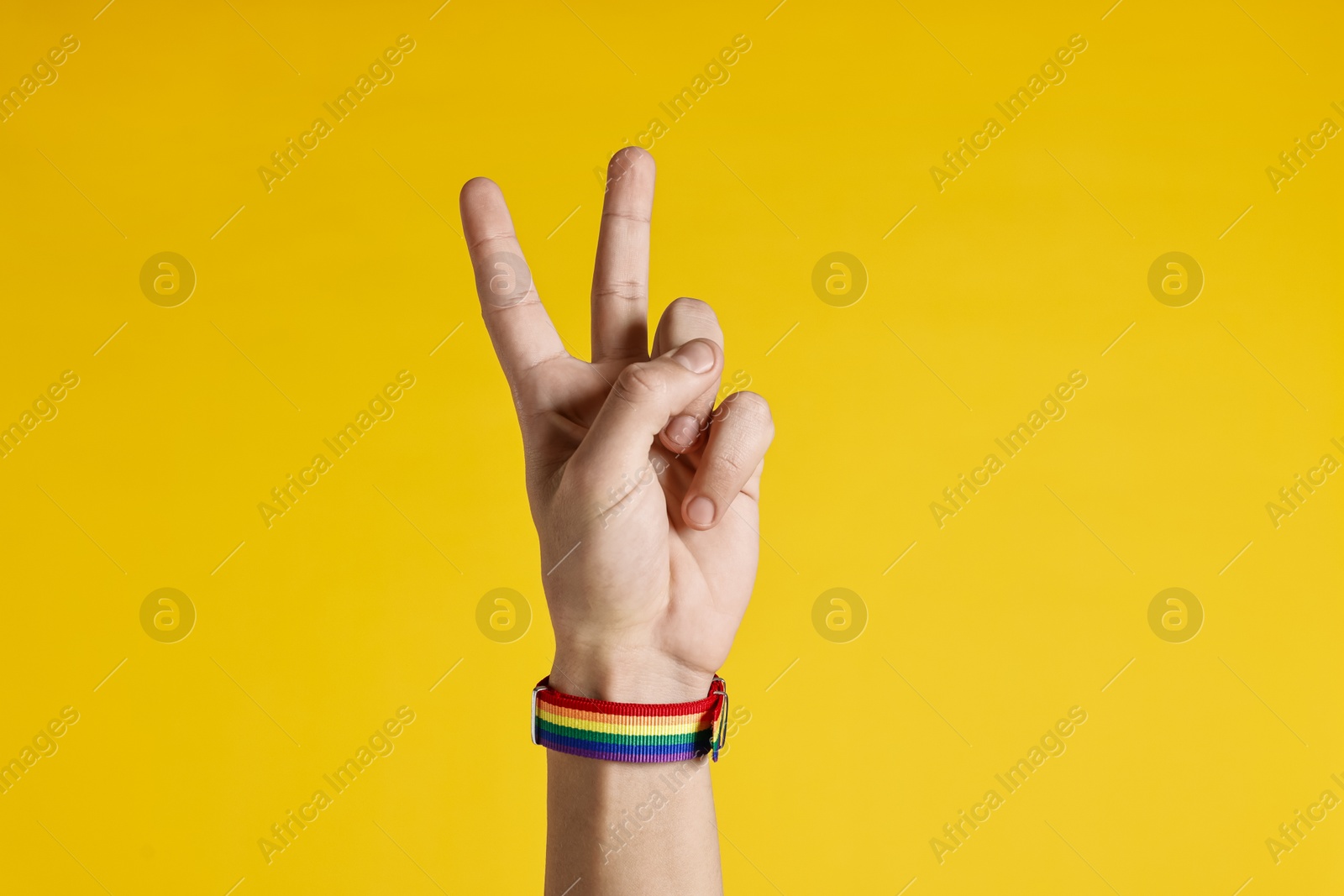 Photo of Man with bracelet in colors of LGBT flag showing peace sign on yellow background, closeup