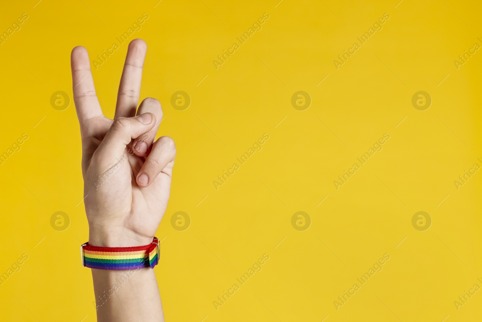 Photo of Man with bracelet in colors of LGBT flag showing peace sign on yellow background, closeup. Space for text