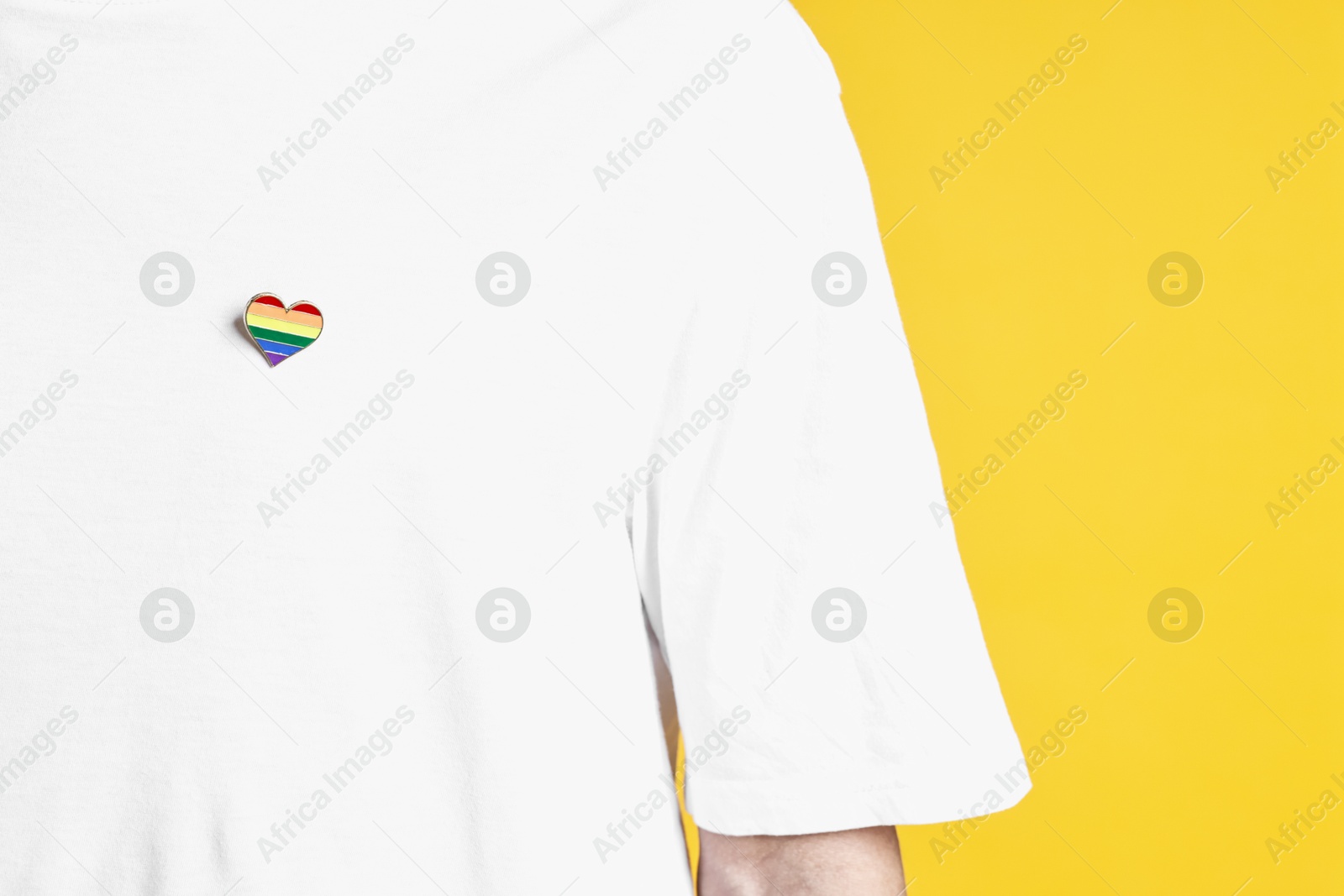 Photo of Man with heart shaped pin in colors of LGBT flag on yellow background, closeup