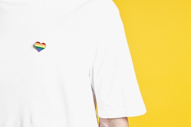 Photo of Man with heart shaped pin in colors of LGBT flag on yellow background, closeup