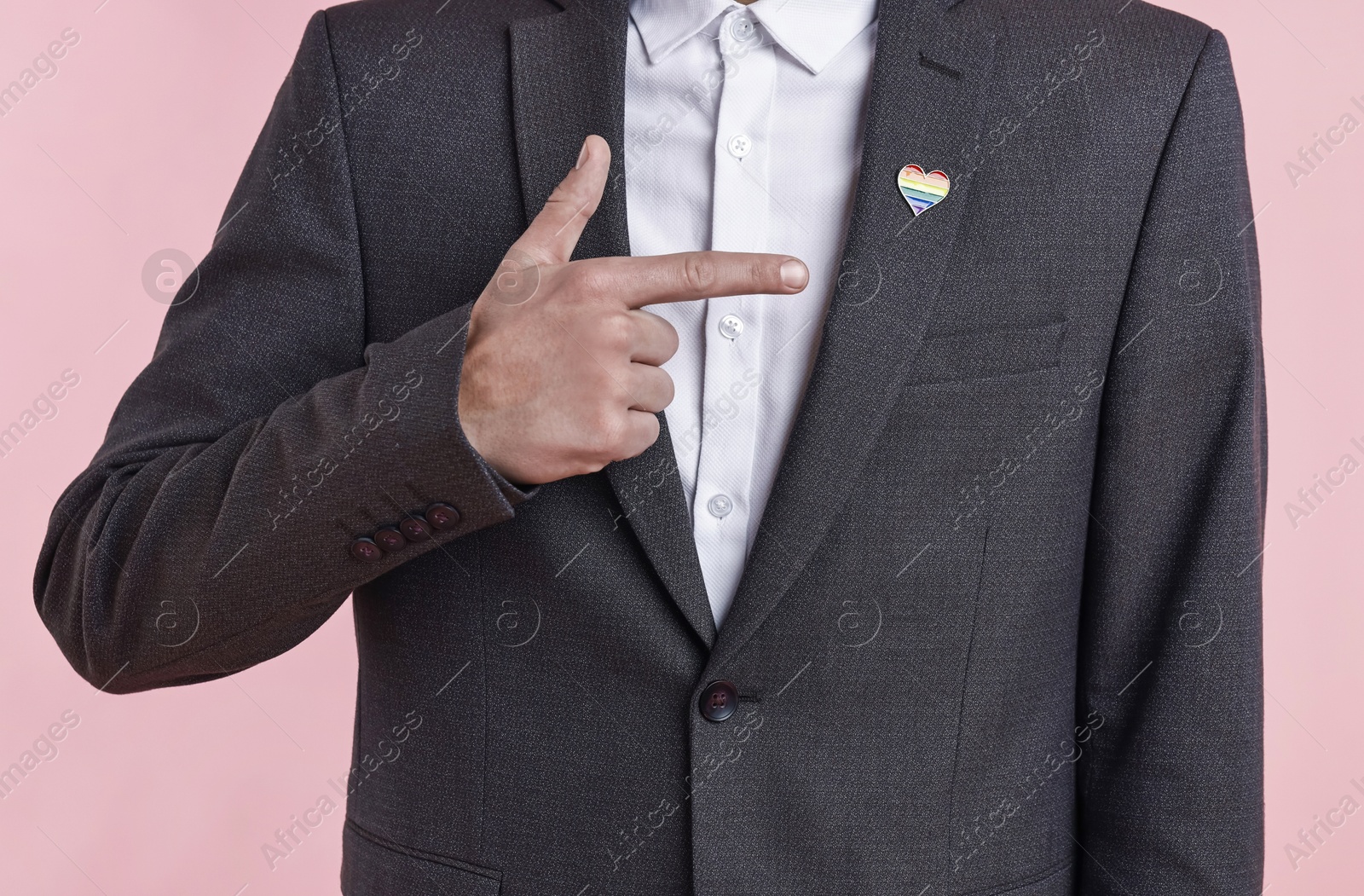 Photo of Man with heart shaped pin in colors of LGBT flag on light pink background, closeup