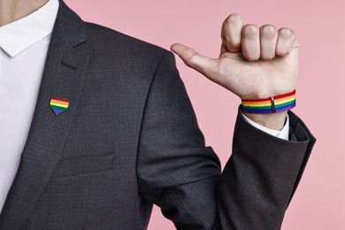 Photo of Man with heart shaped pin in colors of LGBT flag on light pink background, closeup