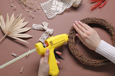 Photo of Woman with hot glue gun making craft on brown background, top view