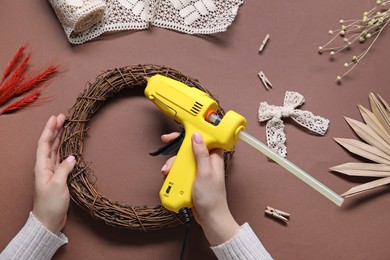 Photo of Woman with hot glue gun making craft on brown background, top view