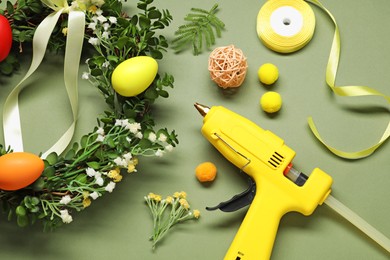 Photo of Hot glue gun and handicraft materials on olive background, flat lay