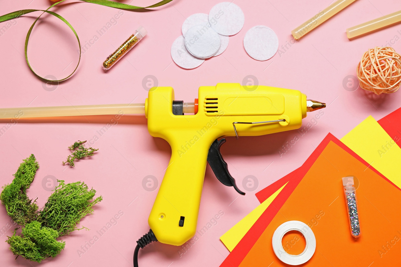 Photo of Hot glue gun and handicraft materials on pink background, flat lay