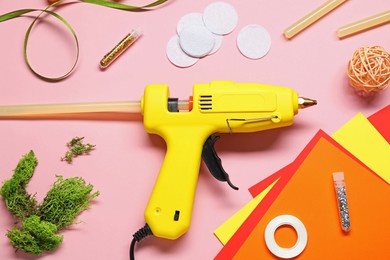 Photo of Hot glue gun and handicraft materials on pink background, flat lay