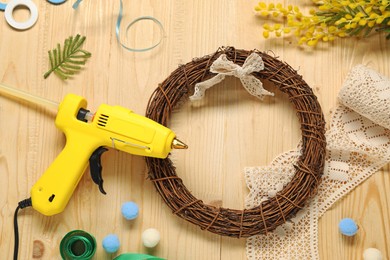 Photo of Hot glue gun and handicraft materials on wooden background, flat lay