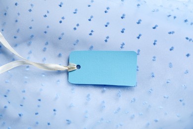 Photo of Blank tag with ribbon on white fabric, closeup