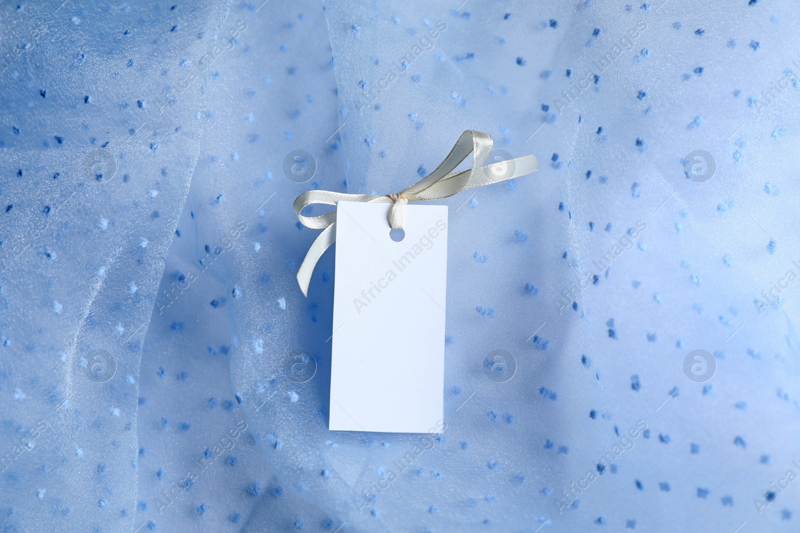 Blank tag with ribbon bow on white fabric, top view Photo of Blank tag with ribbon bow on white fabric, top view