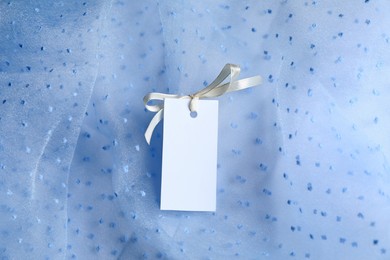 Photo of Blank tag with ribbon bow on white fabric, top view