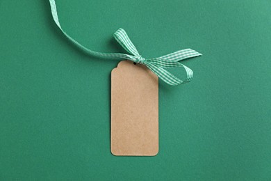 Photo of Blank tag with ribbon bow on green background, top view