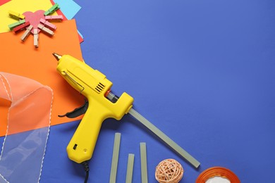 Photo of Hot glue gun and handicraft materials on blue background, flat lay. Space for text