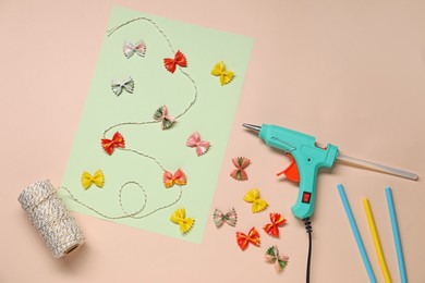 Photo of Hot glue gun and handicraft materials on pink background, flat lay