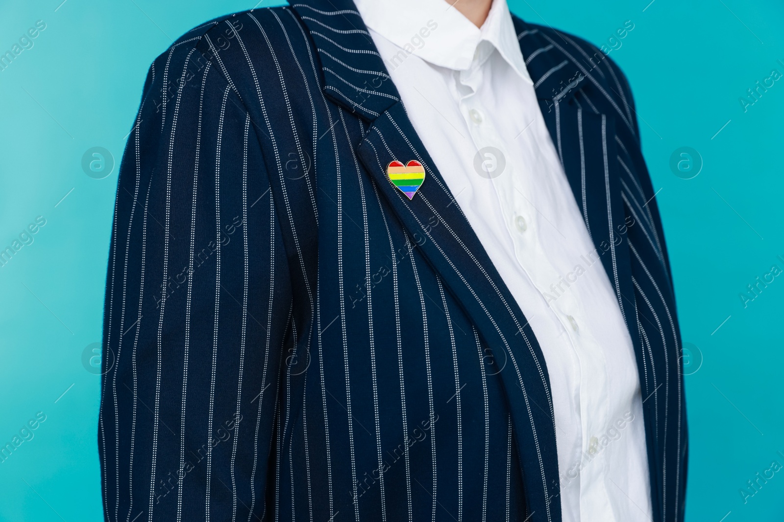 Photo of Woman with heart shaped pin in LGBT colors on light blue background, closeup