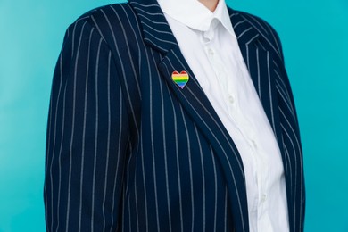 Photo of Woman with heart shaped pin in LGBT colors on light blue background, closeup