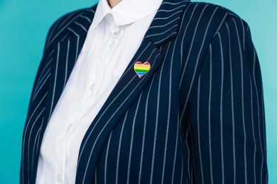 Photo of Woman with heart shaped pin in LGBT colors on light blue background, closeup