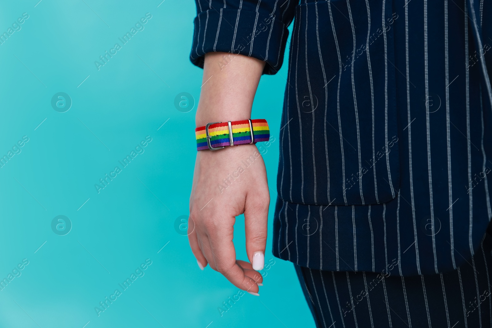 Photo of Woman wearing wristband in LGBT colors on light blue background, closeup. Space for text