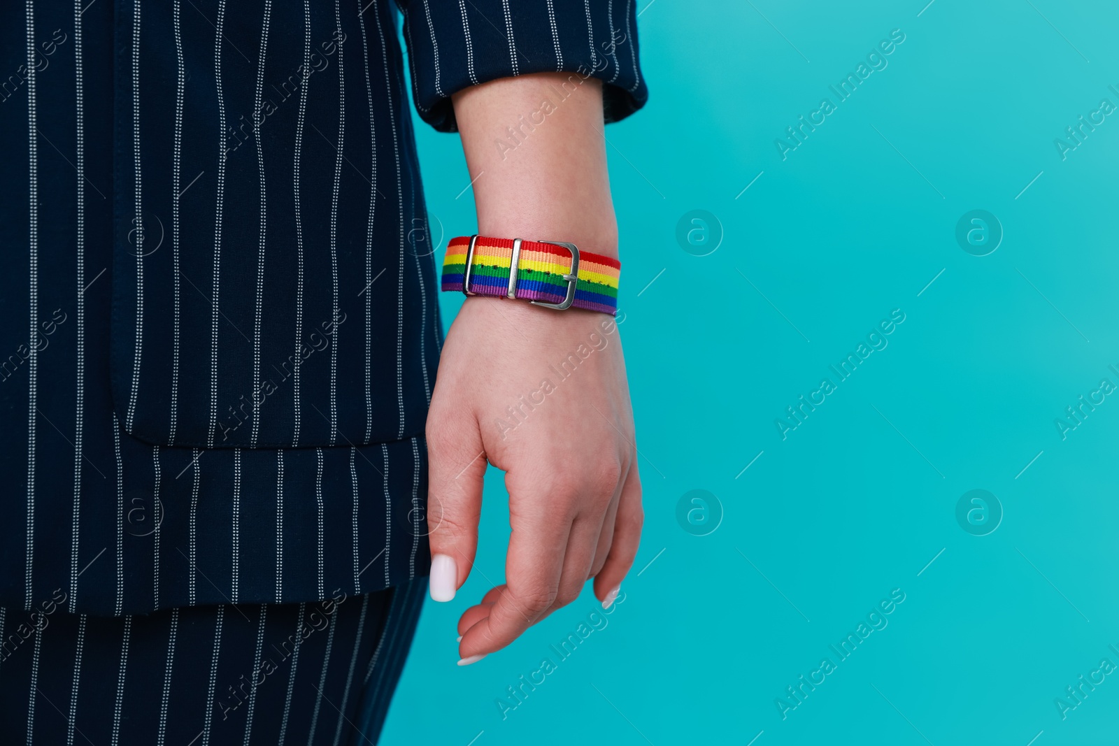 Photo of Woman wearing wristband in LGBT colors on light blue background, closeup. Space for text