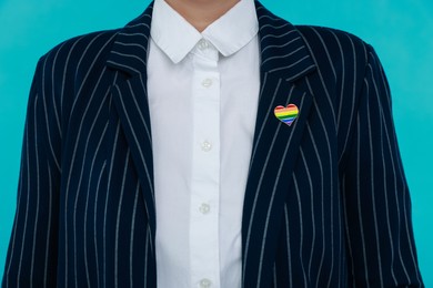 Photo of Woman with heart shaped pin in LGBT colors on light blue background, closeup