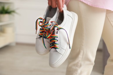 Photo of Woman holding shoes with laces in LGBT colors indoors, closeup