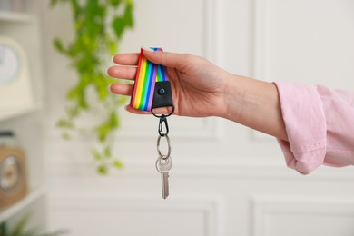 Photo of Woman holding key with keychain in LGBT colors indoors, closeup